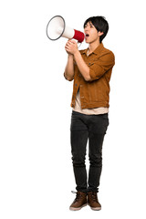 A full-length shot of a Asian man with brown jacket shouting through a megaphone over isolated white background
