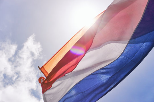 Dutch flag with orange streamer waving in the wind backlit with light leaks and lens flare agains a blue sky and bright sun on Koningsdag. A national holiday in the Kingdom of the Netherlands