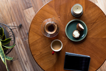 A top down shot of modern living room coffee table with a coffee cup, book, tablet, and a muffin on it.