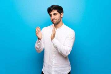 Young man over isolated blue wall applauding after presentation in a conference