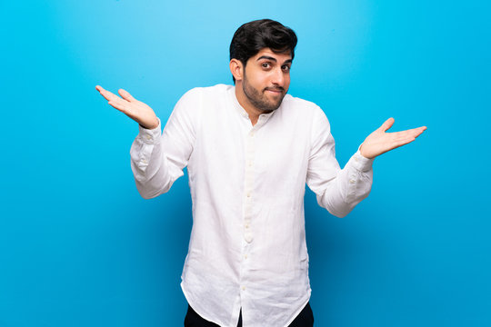 Young man over isolated blue wall making unimportant gesture while lifting the shoulders