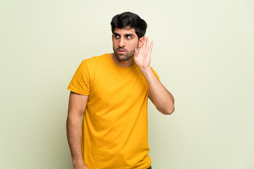 Young man over pink wall listening to something by putting hand on the ear