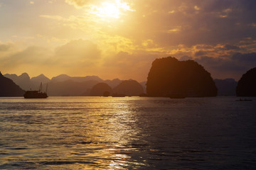 Naklejka na ściany i meble Cruise is a traditional wooden junk sailing rock islands Sunset Background. Vietnam Top Destinations, Ha Long Bay