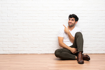 Young man sitting on the floor pointing finger to the side