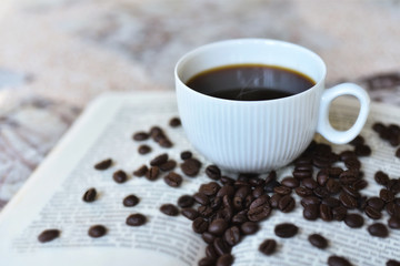 Cup od balck coffee with roasted coffee beans on opened book