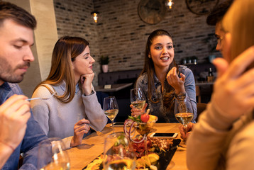 Group of young friends having fun in restaurant, talking and laughing while dining at table.