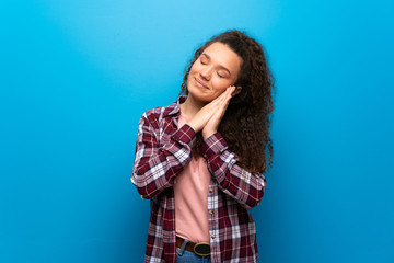 Teenager girl over blue wall making sleep gesture in dorable expression