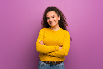 Teenager girl over purple wall keeping the arms crossed in frontal position