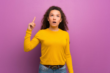 Teenager girl over purple wall thinking an idea pointing the finger up
