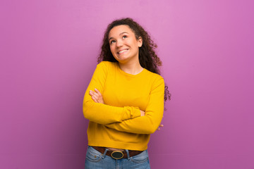 Teenager girl over purple wall looking up while smiling