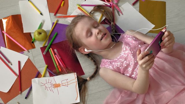 little girl lying on the floor uses the phone, listens to music