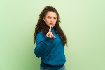 Teenager girl over green wall serious and pointing to the front