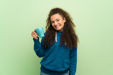 Teenager girl over green wall holding a hot cup of coffee