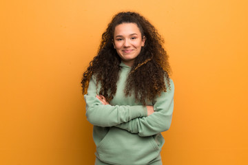 Teenager girl over ocher wall keeping the arms crossed in frontal position