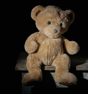 aold brown teddy bear is sitting on a wooden surface