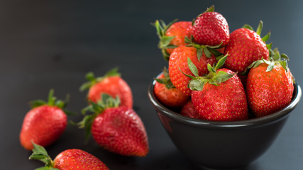 Delicious strawberries in a bowl on black background.