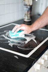 modern house husband cleaning a stove in the kitchen with a sponge and foamy cleaner