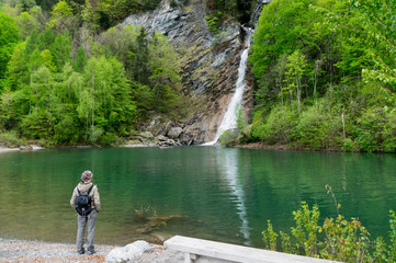 Fototapeta na wymiar woman hiker looking at a beautiful waterfall and colorful swimming pond in green spring forest landscape