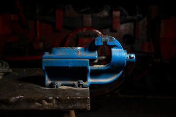 Blue metal mechanical vise mounted on a workbench in the repair shop.