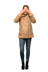 A full-length shot of a Blonde woman with a coat covering eyes by hands. Surprised to see what is ahead over isolated white background