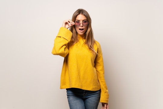 Woman With Yellow Sweater Over Isolated Wall With Glasses And Surprised