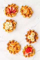 Breakfast with Belgian waffles with strawberry, tangerine and banana topings on marble background top view