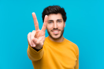 Handsome over isolated blue wall smiling and showing victory sign