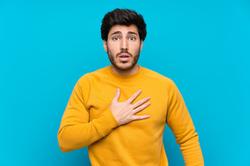 Handsome over isolated blue wall surprised and shocked while looking right