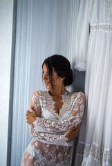 Fototapeta premium Beautiful cheerful happy woman in nightie is standing near a wedding dress. Laugh.