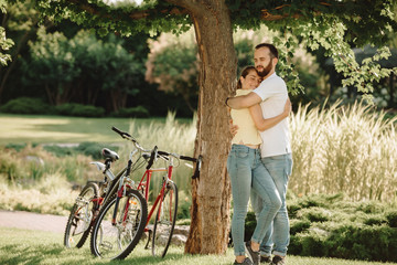Couple in love hugging on summer nature background. Loving man and woman walking in the park on bicycles. Enjoying time spending together.