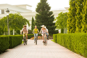Happy students riding bicycles in summer park. Group of cheerful friends ride on bicycles outdoors. Summer holidays with fun.
