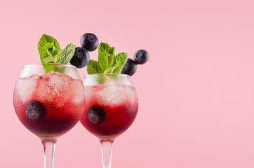 Fresh summer juicy cocktails in two goblets with ice cubes, blueberry, green mint in modern youth pastel soft pink color, copy space, closeup, top section.
