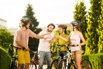 Fototapeta na wymiar Young cyclists playing rock-scissors-paper outdoors. Group of cheerful friends having fun on bicycle ride. Summer tourism concept.
