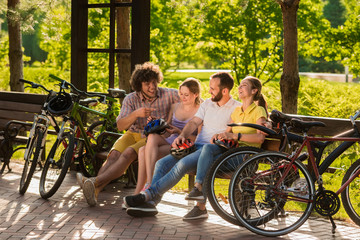 Obraz premium Four friends having rest in park. Group of young cheerful friends spending time together outdoors. Summer weekends of students.