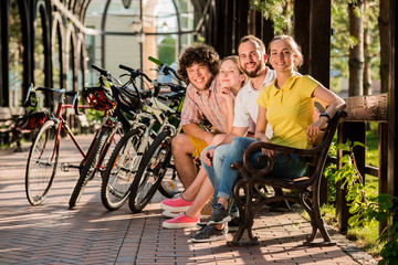 Group of friends having rest in park. Beautiful students in casual outfit resting with bicycles outdoors. Great day for cycling.