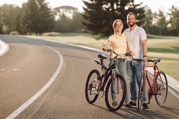 Couple of cyclists is smiling and looking at camera. Happy couple with bicycles outdoors. Romantic date with bikes.