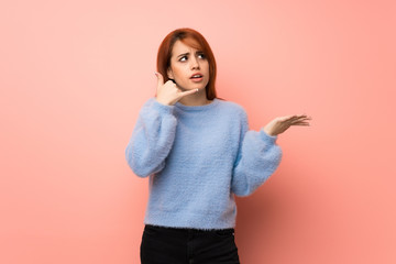 Young redhead woman over pink background surprised and making phone gesture