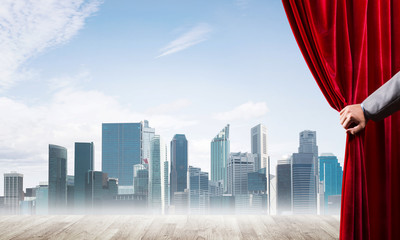 Business city in gray fog behind red curtain and hand holding it