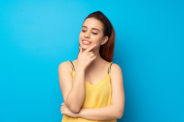 Young redhead woman over blue background looking to the side