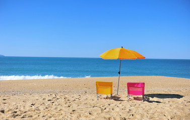 Two colorful beach chairs and umbrella with blue sea water
