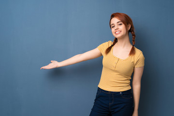 Fototapeta premium Young redhead woman over blue background pointing back and presenting a product