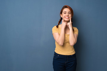 Young redhead woman over blue background smiling with a happy and pleasant expression