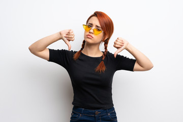Young redhead woman over white wall showing thumb down