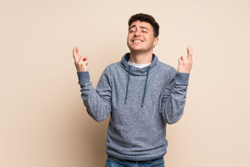 Young man over isolated wall with fingers crossing and wishing the best