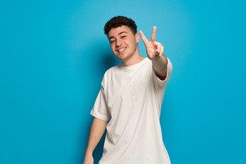 Fototapeta premium Young man over blue background smiling and showing victory sign