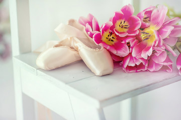 Obraz na płótnie Canvas Pointe shoes with a delicate bouquet of tulips on a white wooden stool. General view.