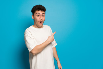 Young man over blue background surprised and pointing side