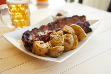 Grilled pork ribs with barbecue sauce, baked potatoes and beer mug.