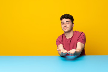 Young man with colorful wall and table holding copyspace imaginary on the palm to insert an ad