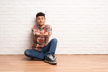 Young man sitting on the floor holding copyspace imaginary on the palm to insert an ad